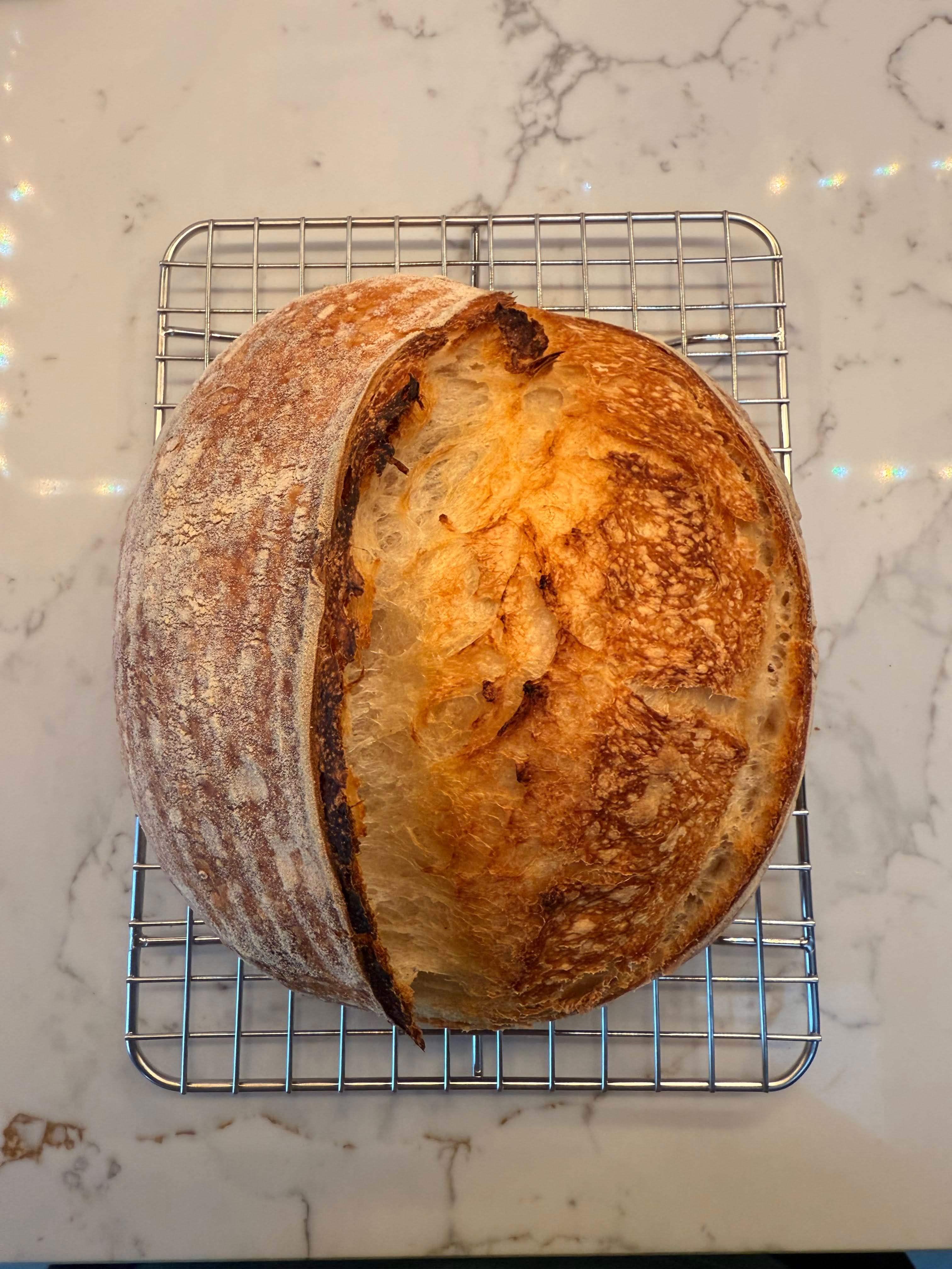 Golden brown round sourdough loaf cooling on a wire rack